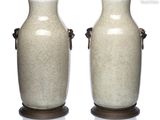 paire de vases munis d'anses, posés sur des socles en bois, sur fond blanc