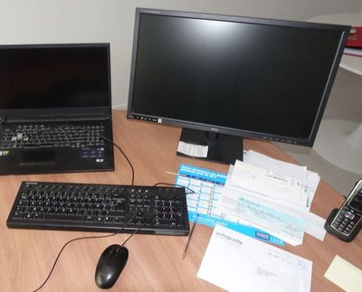 a desk with a laptop, monitor, keyboard and cell phone on it