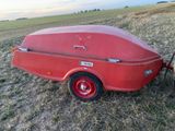un petit bateau rouge sur une remorque, au milieu d'un champ