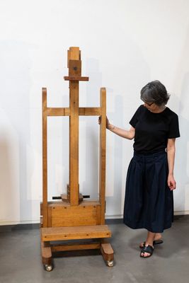 a woman standing next to a wooden easel in a room