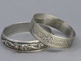 pair of silver bangles with red stones on them on a gray surface