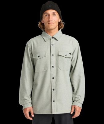 un homme vêtu d'une chemise grise et d'un chapeau noir, debout devant un fond noir