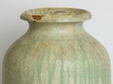a green vase sitting on a table with a white wall in the background
