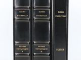 trois livres noirs ornés de lettres dorées, posés sur une surface blanche