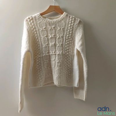 a white sweater hanging on a hanger against a wall