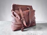 un sac à main en cuir marron posé sur une surface en béton, avec un mur blanc en arrière-plan