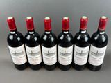 six bottles of red wine lined up in a row on a table