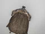 un porte-monnaie argenté entouré d'une chaîne, posé sur une surface blanche