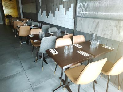 Dans un restaurant, des tables et des chaises sont alignées, avec un mur de briques en arrière-plan.