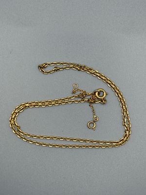 un gros plan d'un collier en or avec une chaîne posé sur une surface grise