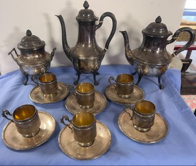 cinq théières en argent et six tasses en argent posées sur une nappe bleue