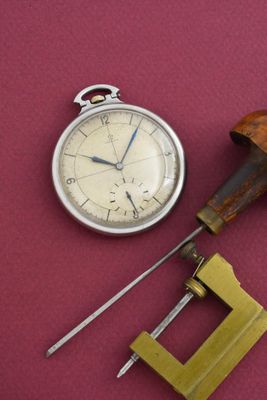 une montre de poche et une paire d'outils posés sur une surface rouge