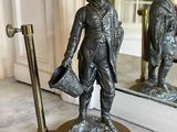 a bronze statue of a man holding a hat and a bag