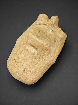 un petit objet en pierre sur lequel est représenté un visage, sur un fond noir