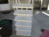 a stack of white shelves on the sidewalk next to a potted plant