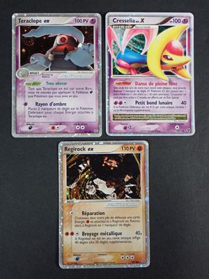 Trois cartes Pokémon sont posées sur une table avec un fond noir.