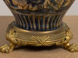 a blue and white vase with a gold base on a table