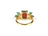 an image of a gold ring with a red stone surrounded by green stones