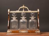 an old fashioned glass decanter with four glass bottles on a wooden stand