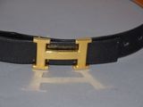 black leather belt with a gold h buckle on a white surface