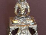 statue en laiton représentant une personne assise sur une table, sur fond marron
