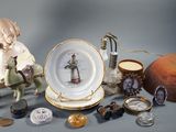 une figurine représentant un garçon assis sur une chaise, à côté d'une assiette et d'autres objets