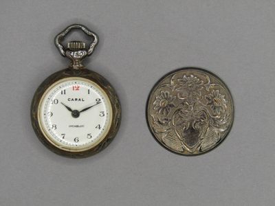 une petite montre de poche en argent à côté d'une pièce de monnaie