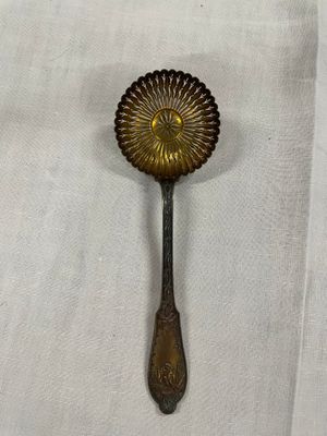 une cuillère en laiton ornée d'un motif floral, posée sur une nappe blanche
