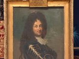 portrait d'un homme en manteau noir, dans un cadre doré, posé sur un tapis rouge