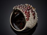 a close up of a ring with a red stone and diamonds