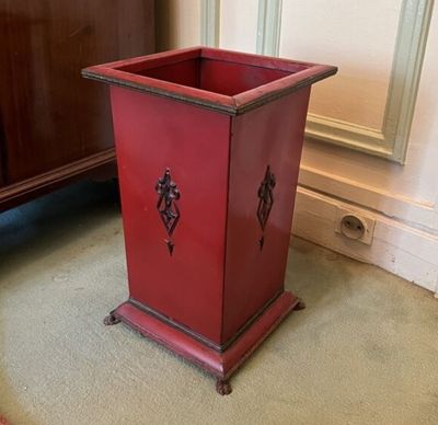 a red planter sitting on the floor in front of a cabinet