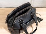 black leather handbag sitting on a wooden table with a white wall in the background