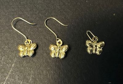 a pair of gold butterfly earrings on a black surface