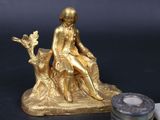 a gold figurine of a woman sitting on a tree stump next to a candle