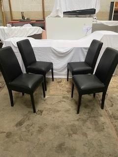 quatre chaises en cuir noir dans une pièce où se trouve une table blanche