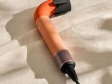 un sèche-cheveux orange posé sur un lit, muni d'un cordon noir