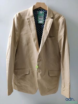 beige jacket hanging on a hanger on a wall with a polka dot shirt underneath it