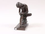 bronze statue of a man sitting on a rock with his head in his hands