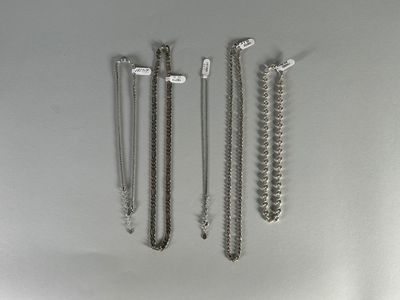 three silver necklaces and two silver bracelets hanging on a wall