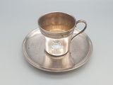 une tasse et une soucoupe en argent posées sur une soucoupe, sur une table