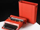 a red typewriter next to a red case on a table