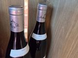 two bottles of wine sitting on a shelf next to each other