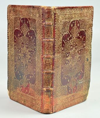 an old book with gold and red covers on a white surface