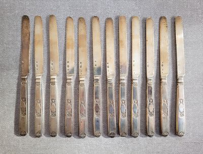 six couteaux anciens en métal argenté et un porte-couteaux posés sur une table