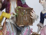 a figurine of a man and a woman holding a bird in a cage