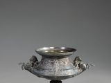 un vase en argent posé sur un socle en bois, lui-même posé sur une surface grise