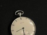 une montre de poche en argent posée sur une surface noire