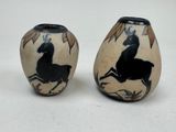 pair of black and white vases with horses on them on a white surface