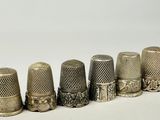 six dés à coudre anciens alignés sur une surface blanche