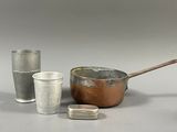 three cups, a saucepan, a spoon and a cup on a table